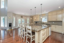 Expansive kitchen featuring a large island with an undermount sink and three pendant lights, ample cabinetry, a tiled backsplash, and wood-finish flooring - 