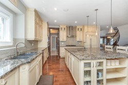 Spacious kitchen featuring an expansive island with seating, light-toned cabinetry, granite countertops, and wood-finish flooring - 