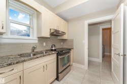 Kitchen featuring light cabinetry with brushed nickel hardware, a stainless steel double basin sink, and a stainless steel oven range with an overhead vent - 