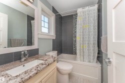 Bathroom featuring a built-in tub with a tile surround, a single vanity with a granite-style countertop, and a window with white trim - 