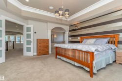 Carpeted bedroom featuring a tray ceiling, contemporary chandelier, and a horizontal striped accent wall - 