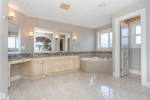 Expansive bathroom featuring dual vanities with granite countertops, an integrated makeup area, a corner soaking tub, and large format tile flooring - 3503 Watson Point(E), Edmonton, AB 