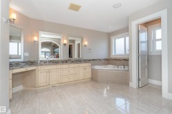 Expansive bathroom featuring dual vanities with granite countertops, an integrated makeup area, a corner soaking tub, and large format tile flooring - 