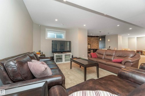Spacious open-concept recreation room featuring recessed lighting, a window with horizontal blinds, and a built-in bar area with stone accent wall and pendant lighting - 3503 Watson Point(E), Edmonton, AB 