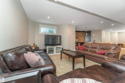 Spacious open-concept recreation room featuring recessed lighting, a window with horizontal blinds, and a built-in bar area with stone accent wall and pendant lighting - 