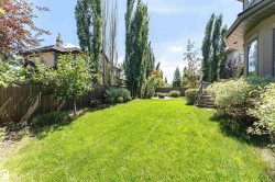 Expansive backyard featuring a manicured lawn, established perimeter fencing, mature trees, and a wooden staircase leading to the property - 