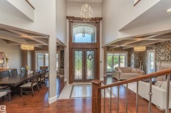 Grand foyer featuring a double-height ceiling, dark wood-finish double entry doors with decorative glass inserts, and a tiled entryway - 