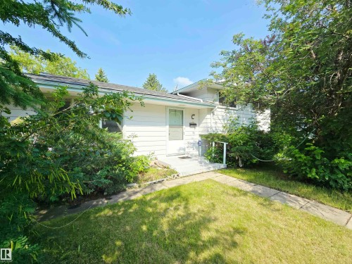 White siding exterior with a dark shingle roof, a front door with a mail slot, a concrete entry pad, and established perimeter landscaping - 5012 143 Street, Edmonton, AB 
