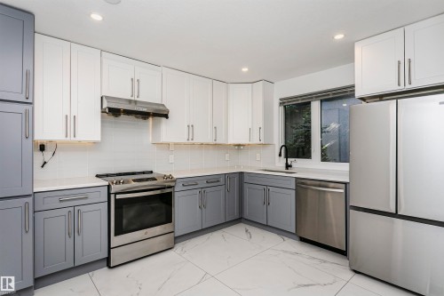 Kitchen featuring two-tone cabinetry with white upper and gray lower cabinets, stainless steel appliances, light-toned countertops, a white subway tile backsplash, and recessed lighting - 17716 84 Avenue, Edmonton, AB 