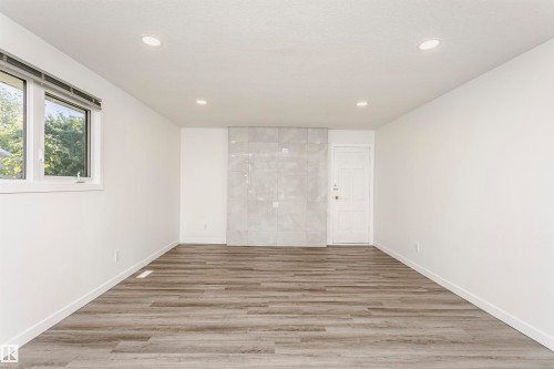 Spacious room featuring wood-finish flooring, a window with exterior views, recessed lighting, a tiled accent wall, and a panel door - 17716 84 Avenue, Edmonton, AB 