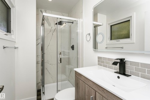 Contemporary bathroom featuring a wood-finish vanity with an integrated sink, matte black faucet, and gray subway tile backsplash - 17716 84 Avenue, Edmonton, AB 