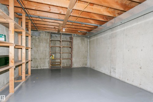 Expansive unfinished lower level featuring exposed wood joists, concrete walls, a gray painted concrete floor, and built-in wood shelving units - 17716 84 Avenue, Edmonton, AB 