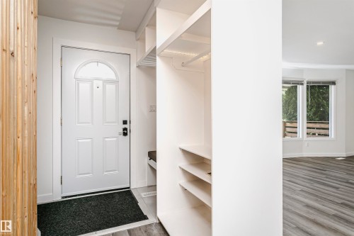 Entryway featuring a white paneled door with an arched transom, wood-finish flooring, built-in open shelving, a built-in bench, and a coat rod - 17716 84 Avenue, Edmonton, AB 