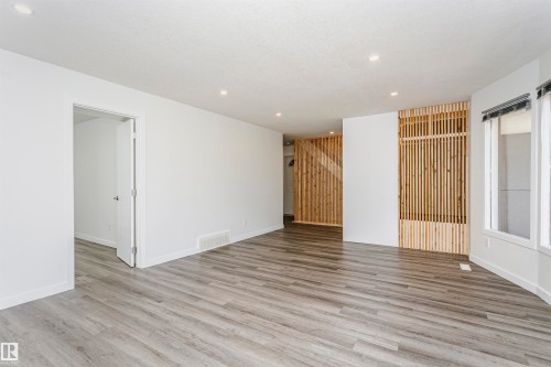 Spacious room featuring light wood-finish flooring, recessed lighting, white walls, and a distinctive wood slat architectural detail - 17716 84 Avenue, Edmonton, AB 
