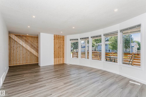 Spacious interior featuring a curved wall of large windows, wood-finish flooring, recessed lighting, and a slatted wood accent wall - 17716 84 Avenue, Edmonton, AB 