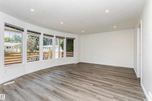 Curved window wall with multiple large panes, overhead recessed lighting, light-toned wood-finish flooring, and white baseboards - 17716 84 Avenue, Edmonton, AB 