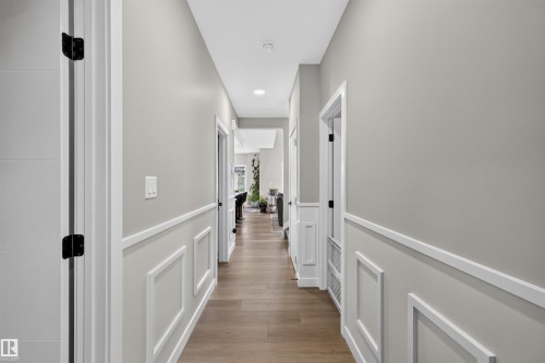 Main Floor Hallway featuring panel molding, light gray walls, wood-finish flooring, white trim, and black door hardware - 1573 Esaiw Place, Edmonton, AB 