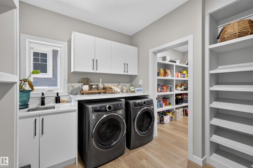 Dedicated utility room featuring light wood-finish flooring, white cabinetry with dark hardware, a countertop with an inset sink, and built-in shelving - 1573 Esaiw Place, Edmonton, AB 