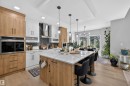 Modern kitchen featuring a large central island with seating, integrated oven, herringbone tile backsplash, and light wood-finish flooring - 1573 Esaiw Place, Edmonton, AB 