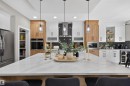 Spacious kitchen featuring a large central island with a light-toned countertop, contrasting white and wood-finish cabinetry, a dark herringbone tile backsplash, and built-in stainless steel appliances - 1573 Esaiw Place, Edmonton, AB 