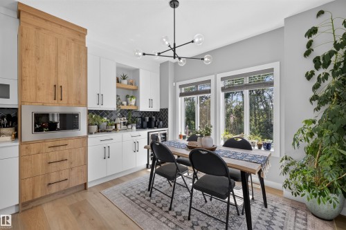 Modern kitchen and dining area featuring white shaker-style cabinetry with matte black hardware, a built-in microwave, wood-finish flooring, and a black geometric chandelier - 1573 Esaiw Place, Edmonton, AB 