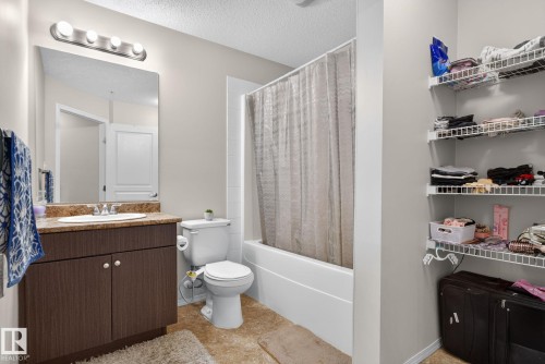 Bathroom featuring a vanity with dark wood-finish cabinetry and a light-colored countertop, a rectangular mirror, and a four-bulb vanity light fixture - 140 301 Clareview Station Drive, Edmonton, AB 