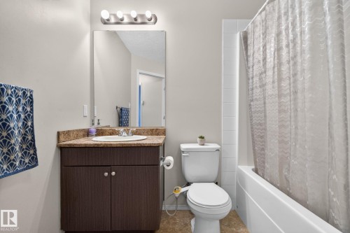 Full bathroom featuring a dark wood-finish vanity with a surface-mount sink, a coordinating countertop, and a wall-mounted mirror with overhead light fixture - 140 301 Clareview Station Drive, Edmonton, AB 