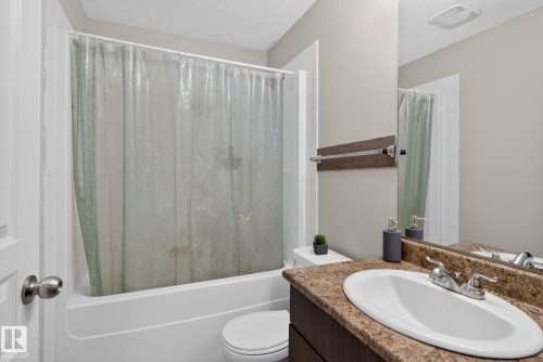 Bathroom featuring a white tub and shower combination, a dark wood-finish vanity with an oval sink, a speckled countertop, and a wall-mounted mirror - 140 301 Clareview Station Drive, Edmonton, AB 