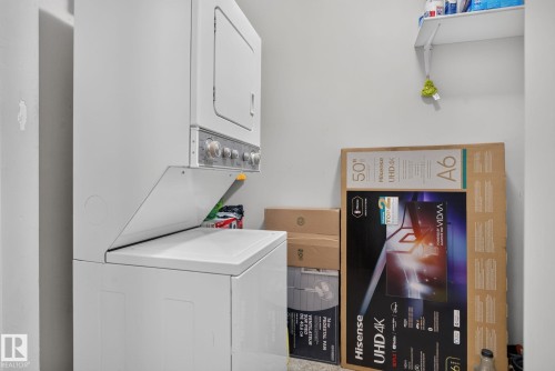 Compact laundry area featuring a stacked washer and dryer unit, white wall shelving, and neutral wall finishes - 140 301 Clareview Station Drive, Edmonton, AB 