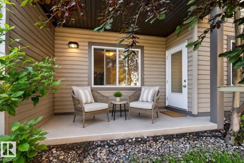 Covered concrete patio featuring horizontal siding, a white door with a glass insert, and a wall-mounted light fixture - 140 301 Clareview Station Drive, Edmonton, AB 