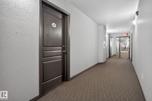 Corridor featuring textured walls, patterned carpeting, a dark wood-finish entry door, and recessed lighting - 140 301 Clareview Station Drive, Edmonton, AB 
