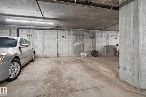 Dedicated parking space within a concrete garage structure, featuring overhead fluorescent lighting and exposed piping - 140 301 Clareview Station Drive, Edmonton, AB 