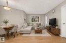 Open-concept living area featuring wood-finish flooring, a contemporary ceiling light fixture, a large window, light-toned walls, and a white door with a silver-tone handle - 140 301 Clareview Station Drive, Edmonton, AB 