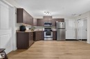 Kitchen featuring wood-finish flooring, dark wood cabinetry, and stainless steel appliances including a refrigerator, range, microwave, and dishwasher - 140 301 Clareview Station Drive, Edmonton, AB 
