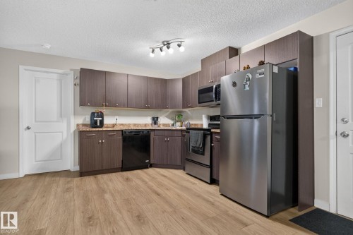 Kitchen featuring dark wood-finish cabinetry, stainless steel refrigerator, black dishwasher, and built-in microwave - 140 301 Clareview Station Drive, Edmonton, AB 