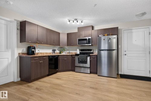Kitchen featuring wood-finish flooring, dark wood-finish cabinetry, stainless steel appliances, and a laminate countertop - 140 301 Clareview Station Drive, Edmonton, AB 