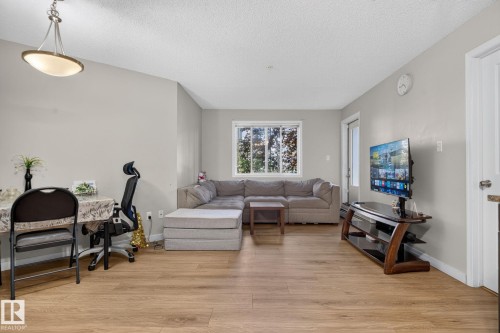 Open-concept living space featuring wood-finish flooring, a contemporary ceiling light fixture, a large window, and light neutral wall paint - 140 301 Clareview Station Drive, Edmonton, AB 