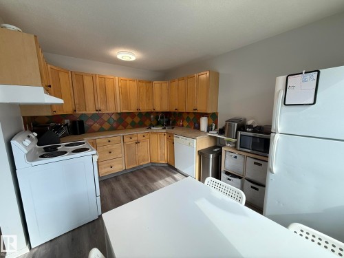 Kitchen featuring wood cabinetry, a colorful tiled backsplash, and wood-finish flooring - 166 Roseland Village, Edmonton, AB - Indoor Photo Showing Kitchen