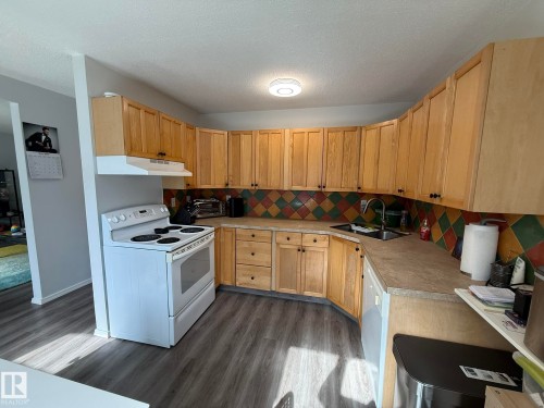 Kitchen featuring extensive light wood cabinetry, a checkered tile backsplash, and wood-finish flooring - 166 Roseland Village, Edmonton, AB - Indoor Photo Showing Kitchen With Double Sink