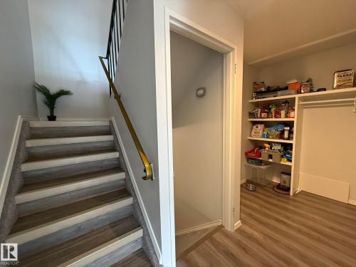 Staircase featuring wood-finish treads with carpet risers, a brass-toned handrail, and black metal balusters - 166 Roseland Village, Edmonton, AB - Indoor Photo Showing Other Room