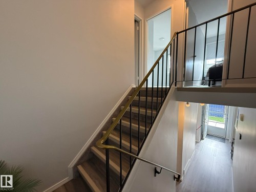 Split-level interior featuring a carpeted staircase with a brass and black metal railing, light gray wall finishes, and wood-finish flooring - 166 Roseland Village, Edmonton, AB - Indoor Photo Showing Other Room