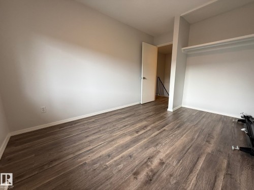 Room featuring wood-finish flooring, light grey painted walls, white trim, and an open closet space with shelving - 166 Roseland Village, Edmonton, AB - Indoor Photo Showing Other Room