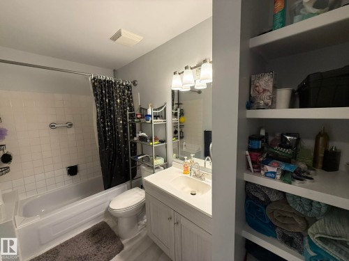 UPPER FLOOR FULL 4pc Bathroom featuring a built-in bathtub with white tile surround, a vanity with an integrated sink and base cabinetry, a wall-mounted mirror, and recessed open shelving - 166 Roseland Village, Edmonton, AB - Indoor Photo Showing Bathroom