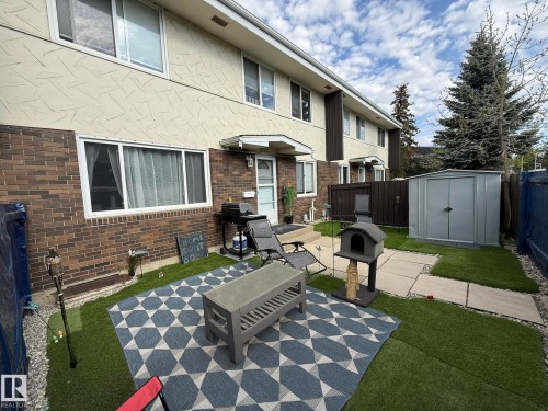 Private fenced rear patio and yard area featuring artificial turf, concrete stepping stones, and a metal storage shed - 166 Roseland Village, Edmonton, AB - Outdoor