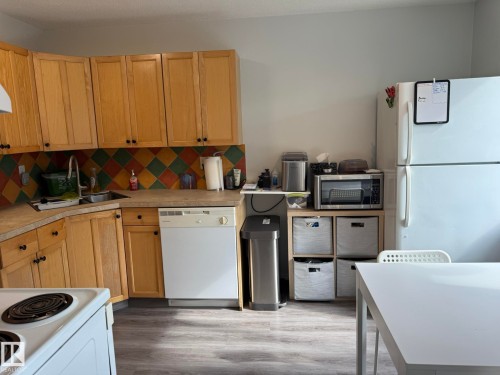 Kitchen featuring wood-finish cabinetry, a tiled backsplash, laminate countertops, a stainless steel sink, and a white dishwasher - 166 Roseland Village, Edmonton, AB - Indoor Photo Showing Kitchen