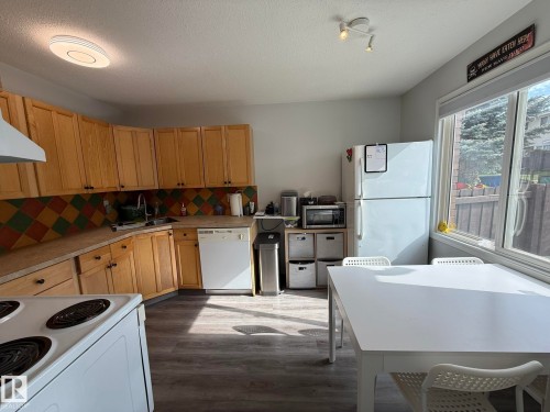 Kitchen featuring wood-finish cabinetry, patterned tile backsplash, and a contemporary ceiling fixture - 166 Roseland Village, Edmonton, AB - Indoor Photo Showing Kitchen