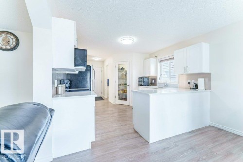 Bright kitchen with white cabinetry, wood-finish flooring, a central island, and a glass-paneled pantry door - 3525 22 Street, Edmonton, AB - Indoor Photo Showing Kitchen