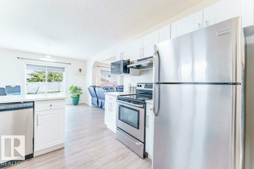 Kitchen featuring stainless steel appliances, white cabinetry, wood-finish flooring, and a window overlooking a fenced backyard - 3525 22 Street, Edmonton, AB - Indoor Photo Showing Kitchen With Stainless Steel Kitchen