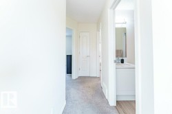 Hallway with light gray carpeting, white baseboards, and white painted walls - 