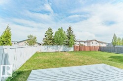 Spacious backyard featuring a white painted wooden fence, diverse mature trees, and a wooden deck area - 
